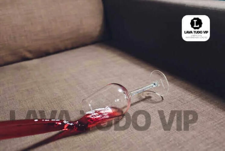 Copo quebrado com vinho tinto derramado sobre sof&aacute; marrom.