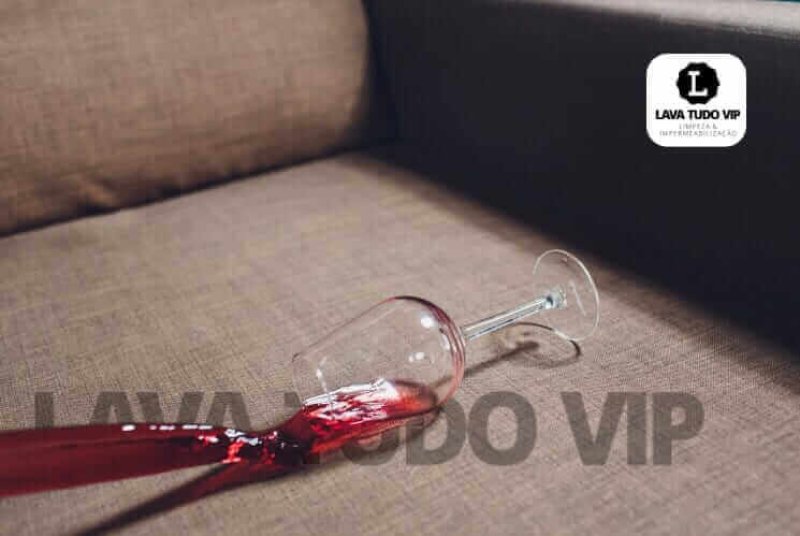 Copo quebrado com vinho tinto derramado sobre sofá marrom.